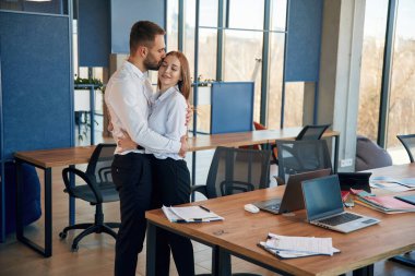 Birbirinize sarılın. Kadın ve erkek çalışanlar ofiste çalışıyor..