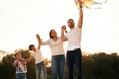 Adam uçurtmayı elinde tutuyor. Tarlada duran babanın, annenin, kızının ve oğlunun aileleri..