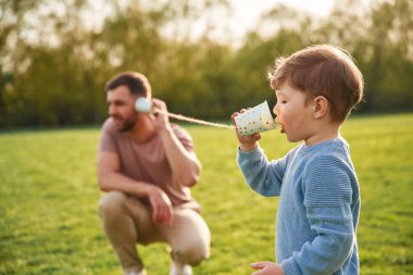 Kağıt bardakta telefonla konuşarak. Mutlu baba ve oğul yazın sahada eğleniyorlar..