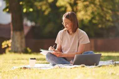 Dizüstü bilgisayarla çimlerin üzerinde. Güzel kız öğrenci üniversitenin yakınında dışarıda..