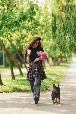 Pembe çiçekler ellerinde. Genç güzel bayan köpeğiyle birlikte parkta..