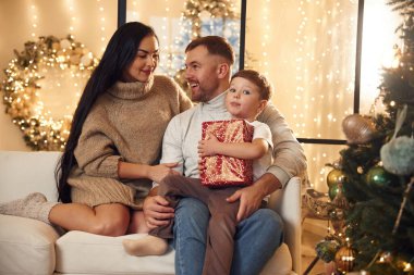 Kırmızı hediye kutusu bir çocuğun elinde. Mutlu bir aile yeni yılı evde kutluyor..