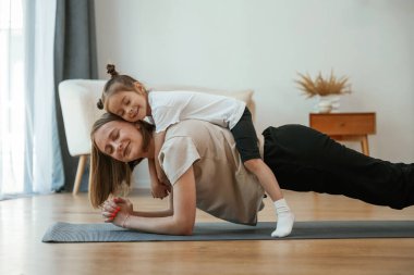 Annemin sırtüstü yatıyorum. Küçük kızı olan genç bir kadın evde yoga yapıyor..