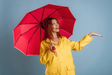 Kırmızı şemsiye ve sarı yağmurluk. Kadın stüdyoda arka planda..