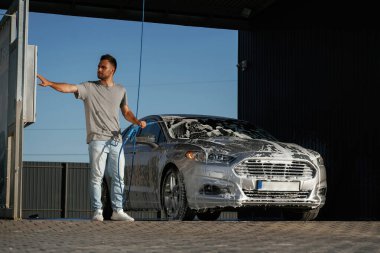 Köpük yıkılıyor, otomobil sabun içinde. Adam dışarıda arabasıyla bekliyor..