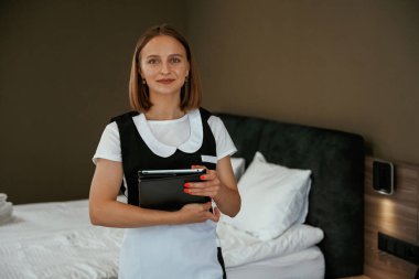 Dijital tablet ellerinde. Genç oda hizmetçisi otel odasında..