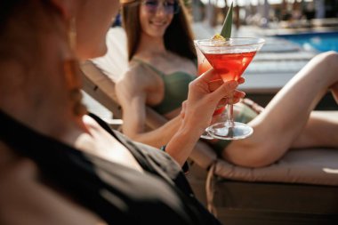 Manzarayı kapat, yan yana otur. İki güzel kadın havuz kenarında dinleniyor..