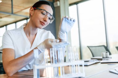 Test tüplerinde sıvı kullanarak kimyasal araştırma. Beyaz önlüklü kadın doktor içeride..