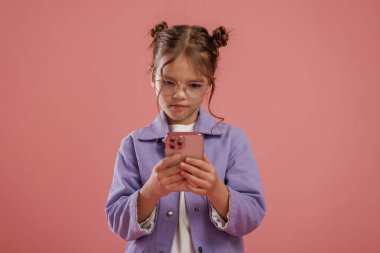 Akıllı telefon kullanarak odaklanmış. Şirin küçük kız pembe arka plana karşı..