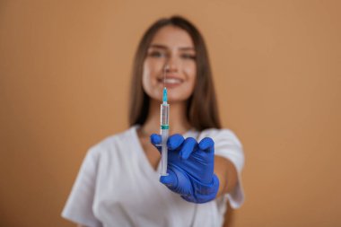 Doktor elinde şırınga tutuyor. Genç ve güzel bir bayan stüdyoda arka plana karşı..