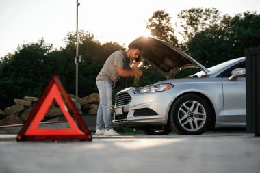 Güneş ışığı altında, kırmızı tabela, kaza, bozuk otomobil, tamir. Adam dışarıda arabasıyla bekliyor..