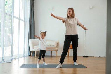 Egzersize odaklan. Küçük kızı olan genç bir kadın evde yoga yapıyor..