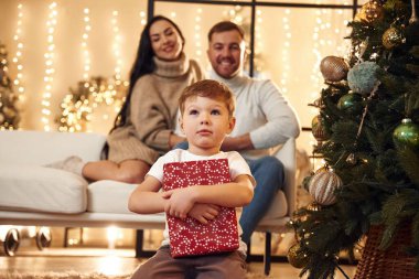 Kırmızı hediye kutusu bir çocuğun elinde. Mutlu bir aile yeni yılı evde kutluyor..