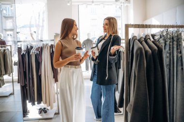 Kadehler el ele. İki bayan arkadaş perakende mağazasında kıyafet seçiyorlar, alışveriş yapıyorlar..