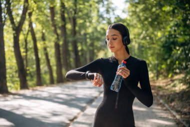 Saate, saate, izleyiciye bakıyorum. Genç, sıska kadın dışarıda siyah spor kıyafetleri giyiyor..