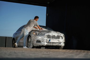 Köpük yıkılıyor, otomobil sabun içinde. Adam dışarıda arabasıyla bekliyor..