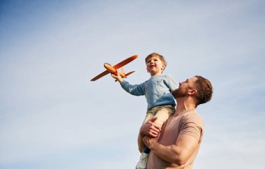 Beyaz bulutlu mavi gökyüzü. Baba oğlunu kucağında tutuyor, oyuncak uçakla oynuyor..