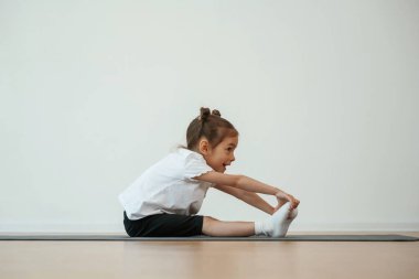 Yan görüş, gerinme. Sevimli küçük kız yoga minderinde oturup egzersiz yapıyor..