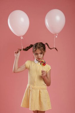 İki balon ve şeker. Şirin küçük kız pembe arka plana karşı..