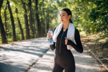 Susuz kalmayın, bir şişe suyla, ayakta. Genç, sıska kadın dışarıda siyah spor kıyafetleri giyiyor..