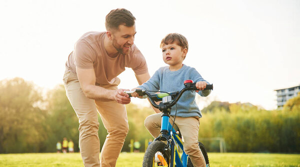 Пробую велосипед. Счастливый отец с сыном веселятся на поле летом.