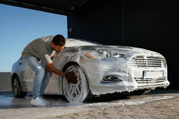 Beyaz sabun ve köpük, otomobili yıkamak. Adam dışarıda arabasıyla bekliyor..