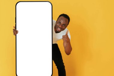 Kopya alanı için çok büyük bir akıllı telefonu var. Siyah adam sarı arka planda stüdyoda..