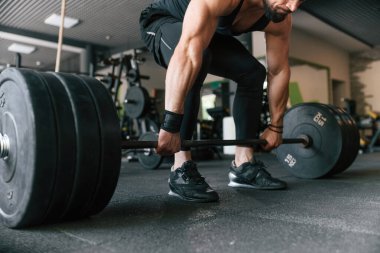 Büyük ve ağır halterler ellerinde. Güçlü kaslı adam spor salonunda çalışıyor..