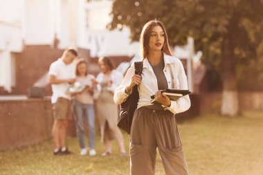Güzel bir kadın arkadaşlarının önünde duruyor. Öğrenci grubu dışarıda..