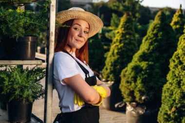 Hasır şapkalı. Genç kızıl saçlı kadın bahçeyle ilgileniyor..