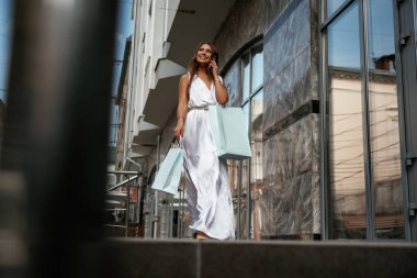 Telefonla konuşmalar. Şık bir kadın alışveriş çantasıyla dışarıda, binanın yanında..