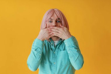 Yüz ifadeleri, el hareketleri. Pembe saçlı adam sarı arka planda poz veriyor..