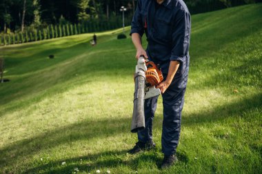 Yaprak üfleyiciyle çalışıyor. Bahçede profesyonel bahçıvan var..