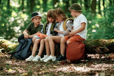 Kamera ve su şişesiyle oturuyor. Çocuklar yazın gündüz vakti ormanda..