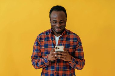 Gülümsüyor ve akıllı telefon tutuyor. Siyah adam sarı arka planda stüdyoda..