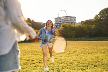 Günlük kıyafetlerle. İki kadın sahada badminton raketleriyle eğleniyor..