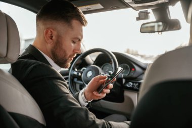 Akıllı telefon kullanarak internette sörf yapmak. Siyah takım elbiseli adam arabada oturuyor..