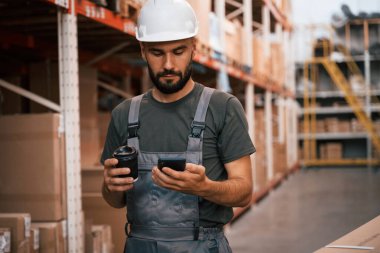 Kahve fincanı ve akıllı telefon ellerinde. Foreman depoda, kargo dağıtım işinde..