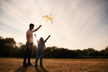 Baba ve oğul, güneş ışığıyla aydınlanan uçurtmayla birlikte sahadalar..