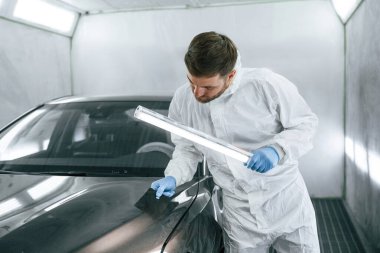 Otomobilin ön tarafında. Garaj çalışanı arabanın aydınlatma ve kontrol yüzeyini tutuyor..