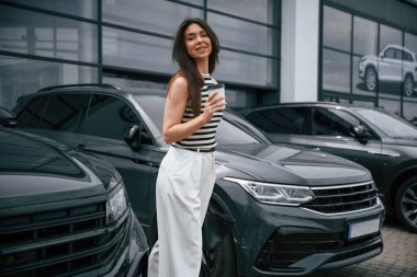 Bir fincan kahve tutuyorum. Çekici genç bayan dışarıda, yepyeni arabasının yanında..