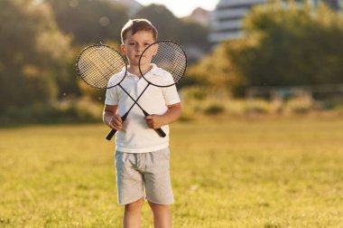 Küçük mutlu çocuk iki tenis ya da badminton raketi ile yaz sahasında.
