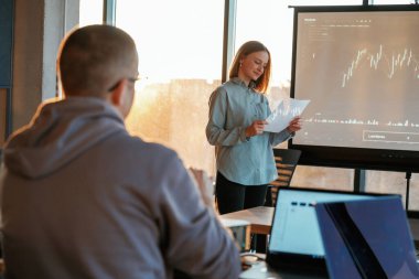 Adam dinliyor. Kadın iş eğitmeni, projektöre karşı iş verileri ile, adama öğretiyor..