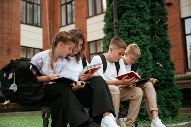 Bankta oturuyor. Çocuklar okulun yanında, öğrenciler..