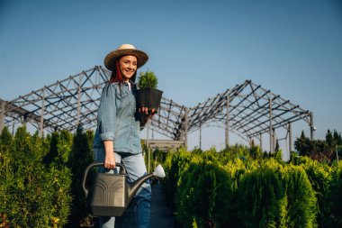Su bidonu. Genç kızıl saçlı kadın bahçeyle ilgileniyor..