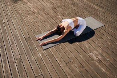Güneş ışığıyla aydınlatılıyor, yoga yapıyor. Spor elbiseli genç bayan dışarıda..
