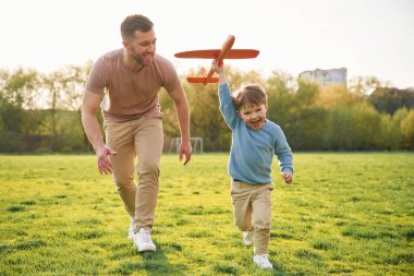 Oyuncak uçak elinde, koşuyor. Mutlu baba ve oğul yazın sahada eğleniyorlar..