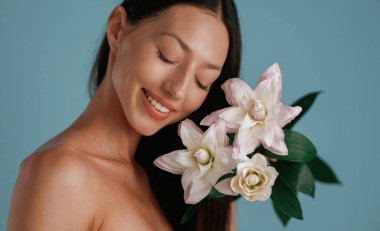 Elinde zambak çiçekleri olan bir portre. Genç kadın stüdyoda arka planda..