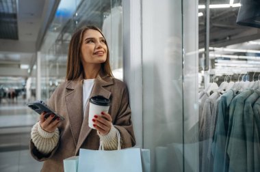 Bir fincan kahve ve telefon ellerde. Alışveriş merkezinde güzel bir kadın var, alışveriş anlayışı..