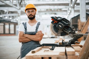 Kollarını kavuşturmuş duruyorsun. Ahşap depoda sanayi işçisi..